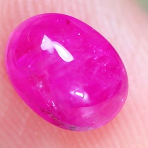 May include: A vibrant, oval-shaped, hot pink gemstone. The polished surface reflects light, creating bright highlights. The gem's color is a saturated, vivid pink, with a smooth, glossy finish. The stone is likely a cabochon cut, suitable for jewelry.