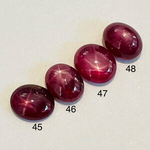 Peut inclure: Quatre pierres précieuses ovales rouge foncé avec un effet d'étoile. Les pierres polies sont numérotées 45, 46, 47 et 48. Les gemmes ont une finition brillante sur un fond clair.