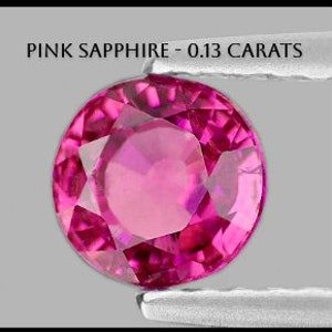 May include: A round, pink sapphire gemstone held in tweezers. The gemstone is 0.13 carats.