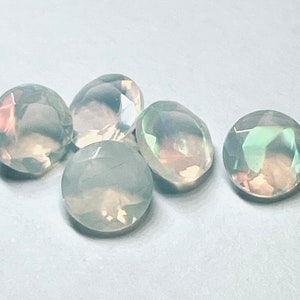 May include: Five iridescent white opal gemstones with a faceted cut. The gemstones are round and have a slight rainbow sheen.