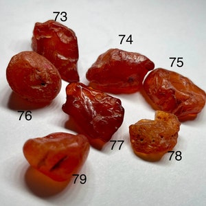 May include: Eight carnelian stones of varying sizes and shapes, ranging in colour from deep red to orange. The stones are numbered 73 through 79.