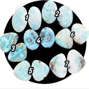 Peut inclure: Une collection de sept pierres précieuses de larimar polies, chacune avec des motifs et des nuances de bleu et de blanc uniques. Les pierres sont numérotées et de formes variées.