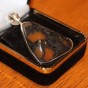 May include: A silver pendant with a brown and green agate stone. The stone has a unique pattern of brown, green, and black.