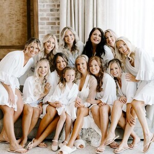 May include: A group of women and a young girl wearing white robes and sandals, sitting on a couch. They are smiling and looking at the camera.