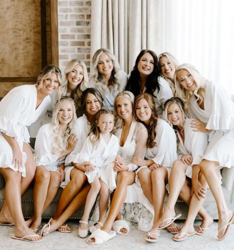 May include: A group of women and a young girl wearing white robes and sandals, sitting on a couch. They are smiling and looking at the camera.
