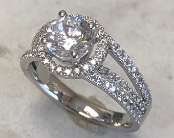 May include: A silver ring with a large, round, clear center stone surrounded by smaller stones. The band is split into two parts, each with a row of smaller stones.