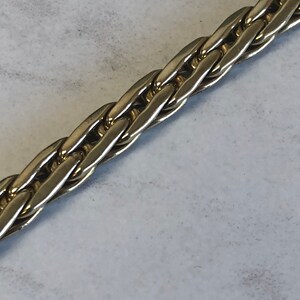 May include: Close-up of a silver chain necklace with a braided design.