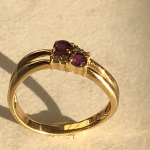 May include: A gold band ring with two oval-shaped purple gemstones and a smaller clear gemstone.