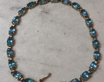 May include: A gold chain bracelet with oval-shaped blue gemstones. The bracelet has a clasp closure.