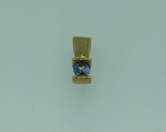Pode incluir: Um pingente de ouro com uma pequena gema azul engastada em uma moldura de ouro.