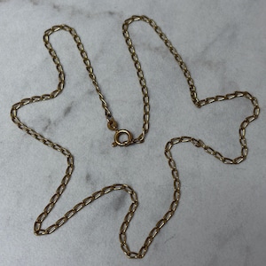 May include: A gold-toned metal chain necklace featuring elongated oval links. The necklace is secured with a circular spring ring clasp, which includes a small, circular metal tag attached near the closure mechanism.