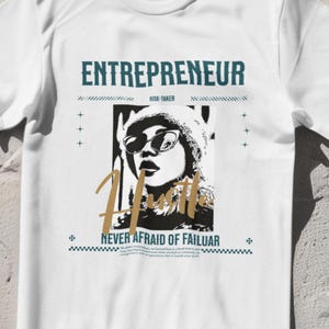 May include: White t-shirt with a graphic design featuring the word "ENTREPRENEUR" in teal, a black and white image of a person wearing sunglasses, and the word "Hustle" in gold. The text "NEVER AFRAID OF FAILUAR" is also included.