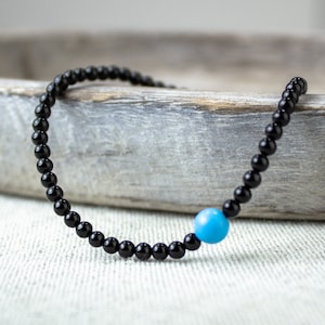 May include: A black beaded bracelet with a single turquoise blue bead.