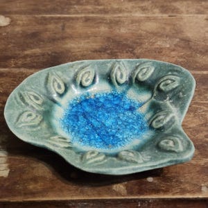 May include: A handcrafted, ceramic dish with a unique, organic shape. The dish features a turquoise exterior and a vibrant, crackled blue interior. Decorative leaf-like patterns adorn the rim, adding a touch of elegance to this decorative piece.