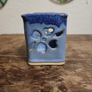 May include: A blue ceramic candle holder with a white base and a cutout flower design.