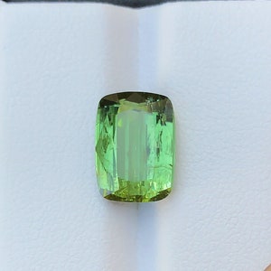 May include: A green gemstone with a rectangular cut, displayed in a white box with a black border.