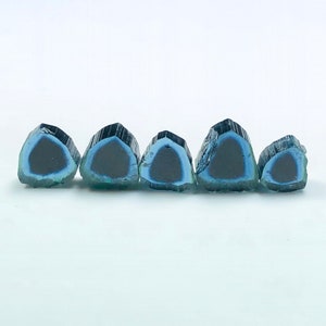 Op de afbeelding: Zes blauwe en zwarte toermalijn edelstenen, gesneden in een driehoekige vorm, zijn in een rij op een wit oppervlak gerangschikt.