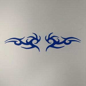May include: A symmetrical blue decal featuring two mirrored tribal-style flame patterns. Each side consists of sharp, curved lines that taper to points, creating a fluid, abstract design that is centred and horizontally aligned on a plain surface.