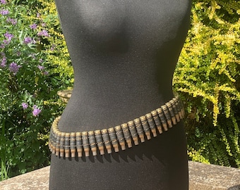 May include: A black mannequin wearing a belt made of linked bullet casings. The belt is wrapped around the mannequin's waist.