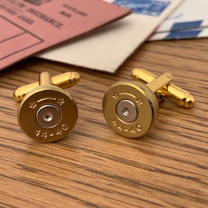 May include: A pair of gold cufflinks shaped like bullet casings. The casings are engraved with the text "44-40".