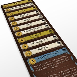 May include: A close-up of a stack of board game cards. The cards have a brown border with text and illustrations. The cards are labeled with names like "Hoard", "Grand Market", and "Watchtower". The cards have a treasure chest icon.