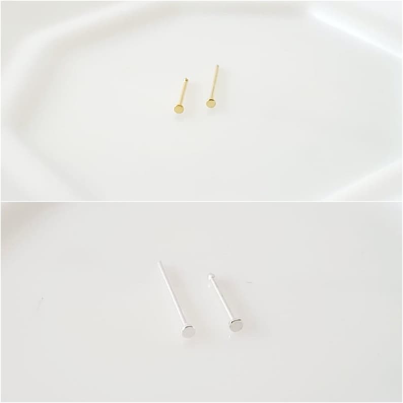 May include: Two pairs of nose rings, one pair is gold and the other is silver. The nose rings are simple and have a small round stud.