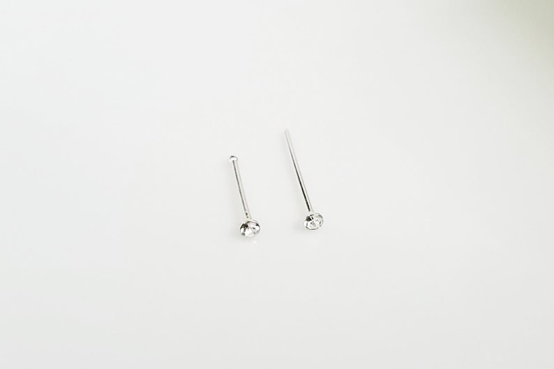 May include: Two silver nose rings with clear rhinestones. The rings are straight and have a simple design.