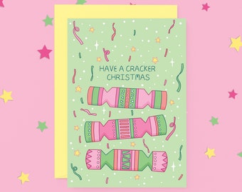 Puede incluir: Una tarjeta de Navidad verde con un borde amarillo. La tarjeta tiene un mensaje festivo que dice "Have a Cracker Christmas" y presenta tres crackers de Navidad ilustrados con diseños rosa y verde.