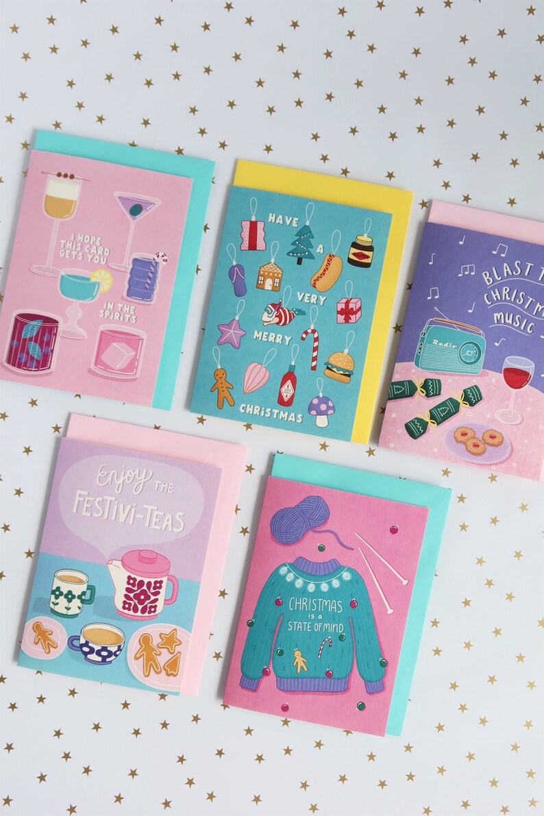 Pu&ograve; includere: Cinque biglietti d'auguri di Natale con diversi design. Le carte sono rosa, blu, gialle, viola e verdi. Le carte presentano illustrazioni di cocktail, ornamenti, tazze da t&egrave;, un maglione e una radio.