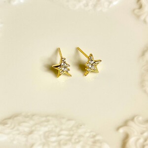 May include: A pair of gold star-shaped earrings with clear cubic zirconia stones.