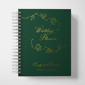 May include: A green spiral bound wedding planner with gold foil lettering that says "Wedding Planner" and "Emily and Daniel Wedding Planner". The cover features a gold foil design of vines and leaves.