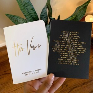 May include: Two white and black cardstock covers with gold lettering. The white cover has the text "Her Vows" and the date "May 15, 2021". The black cover has a quote from 1 Corinthians 13:4-8 about love.