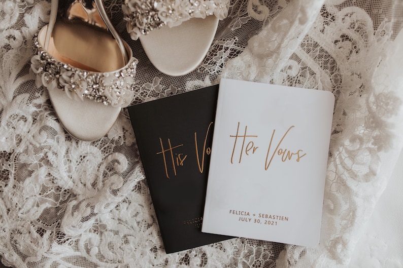 May include: Two white satin bridal shoes with jeweled embellishments and two small black and white books with gold lettering that reads "His Vows" and "Her Vows". The books also include the names "Felicia + Sebastien" and the date "July 30, 2021".