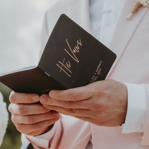 May include: A black booklet with gold lettering that reads "His Vows" and the text "Felica + Garrett April 2022".