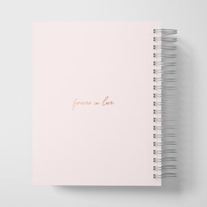 May include: A pink spiral bound notebook with the words "forever in love" written in rose gold lettering.