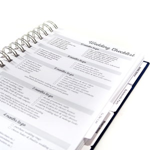 May include: A wedding checklist planner with a spiral binding and tabs for different sections. The checklist includes tasks for 12 months, 9 months, 6 months, 5 months, and 4 months before the wedding.