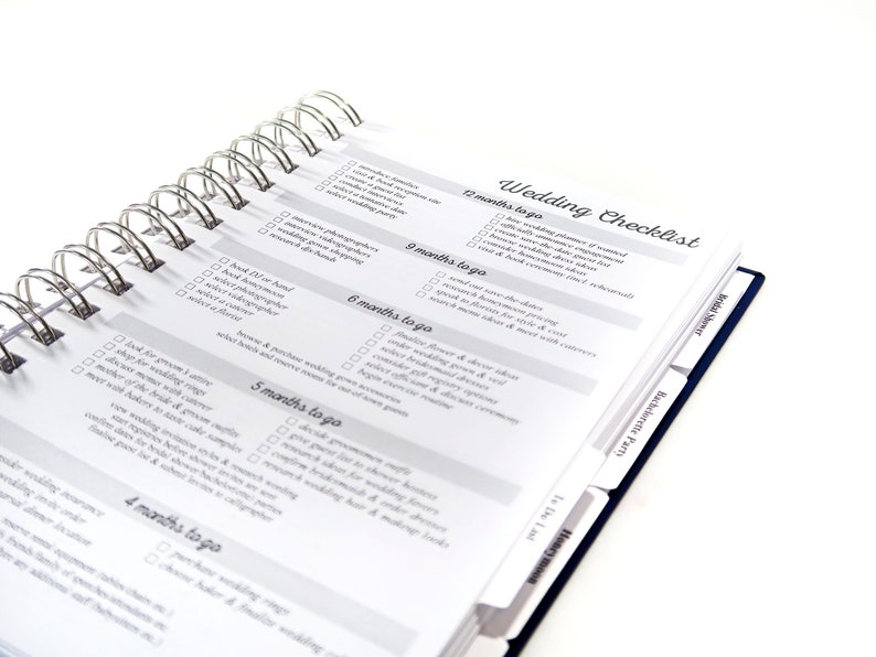 May include: A wedding checklist planner with a spiral binding and tabs for different sections. The checklist includes tasks for 12 months, 9 months, 6 months, 5 months, and 4 months before the wedding.