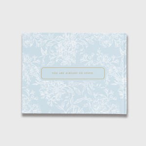 May include: A light blue floral patterned book with the text "YOU ARE ALREADY SO LOVED." The book has a rectangular shape and a gold border around the text. The floral pattern is white.