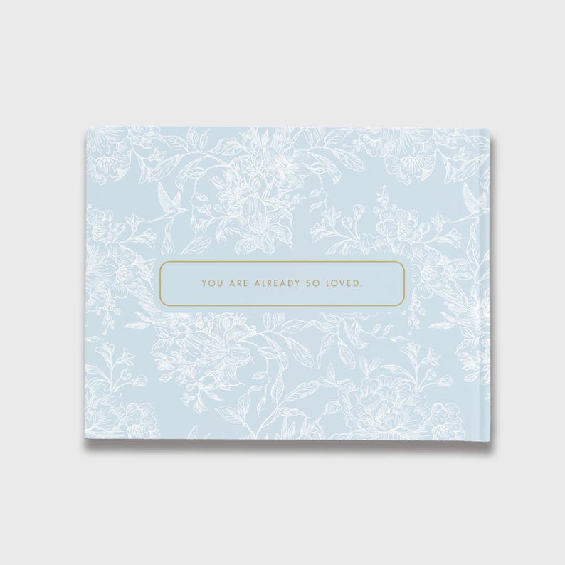 May include: A light blue floral patterned book with the text "YOU ARE ALREADY SO LOVED." The book has a rectangular shape and a gold border around the text. The floral pattern is white.