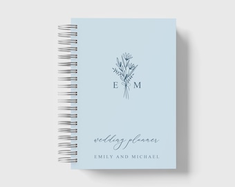Può includere: Un planner di nozze blu chiaro con un design floreale e le iniziali "E & M" al centro. Il testo "wedding planner" e "Emily and Michael" è stampato sotto il design.