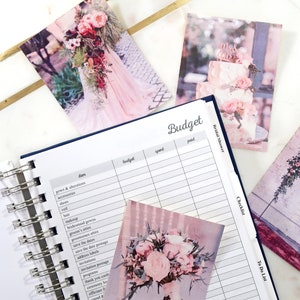 May include: A wedding budget planner with a checklist and to-do list. The planner has a white background with black text and lines. The planner is open to the budget page. There are several photos of wedding decorations on the pages of the planner.