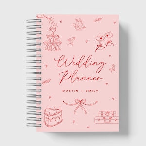 May include: Pink wedding planner with a spiral binding. The cover features red illustrations of champagne glasses, a cake, a suitcase, and a bird. The text "Wedding Planner" and "Dustin + Emily" is printed in red.