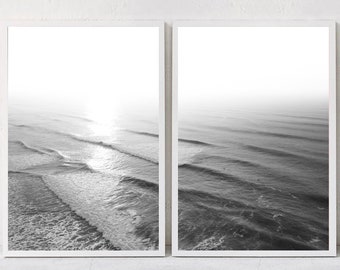 Può includere: Due stampe incorniciate in bianco e nero dell'oceano. La stampa a sinistra mostra le onde con un luminoso riflesso del sole. La stampa a destra mostra l'oceano con dolci onde. Le stampe sono in cornici bianche. Il testo "Paula's Gallery" si trova nell'angolo in basso a destra.