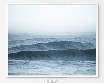 May include: A framed print of ocean waves in shades of blue and gray. The image captures the movement of the water with rolling waves under a hazy sky. The text "Paula's Gallery" is visible in the bottom right corner.