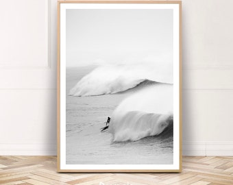Puede incluir: Una fotografía en blanco y negro de un surfista montando una ola grande. La ola está rompiendo y creando una salpicadura de agua. El surfista está silueteado contra el agua blanca.