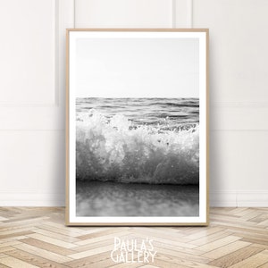 Puede incluir: Fotografía en blanco y negro de una ola rompiendo en la orilla. La ola se rompe en una cresta espumosa, y el agua brilla a la luz del sol.