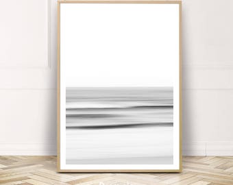 Può includere: Stampa artistica incorniciata in bianco e nero con un'astratta rappresentazione di onde oceaniche. L'immagine sfocata crea un effetto di movimento. La cornice è in legno chiaro e la stampa è esposta su una parete bianca. Design minimalista.