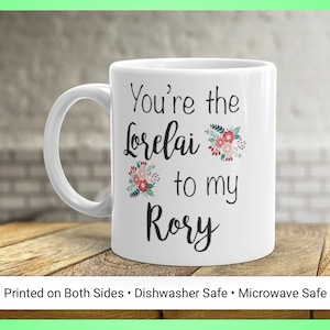 May include: White ceramic mug with the text "You're the Lorelai to my Rory" in black script, accented with floral designs. The mug has a curved handle and the text "Printed on Both Sides • Dishwasher Safe • Microwave Safe" at the bottom.