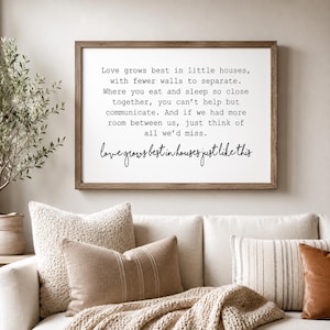 May include: A rectangular wall sign with a brown wooden frame and a white background featuring black text that reads: Love grows best in little houses, with fewer walls to separate. Where you eat and sleep so close together, you can't help but communicate. And if we had more room between us, just think of all we'd miss. Love grows best in houses just like this.