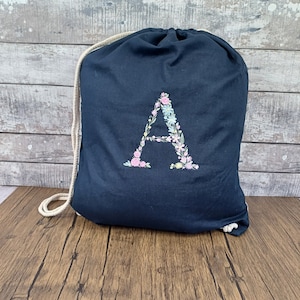 May include: A black drawstring bag with a floral embroidered letter A in pink, blue, and green.